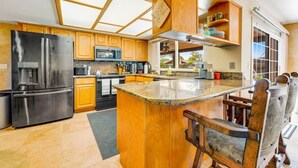 A modern kitchen with wooden cabinets, stainless steel appliances, and a large island. - Backyard Oasis Ideal for Spring/Summer! Pool, Misters, Bluetooth Speakers + more (Mesa)