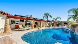 A pool area with a curved pool, lounge chairs, and a building with large windows and stone pillars. - Backyard Oasis Ideal for Spring/Summer! Pool, Misters, Bluetooth Speakers + more (Mesa)