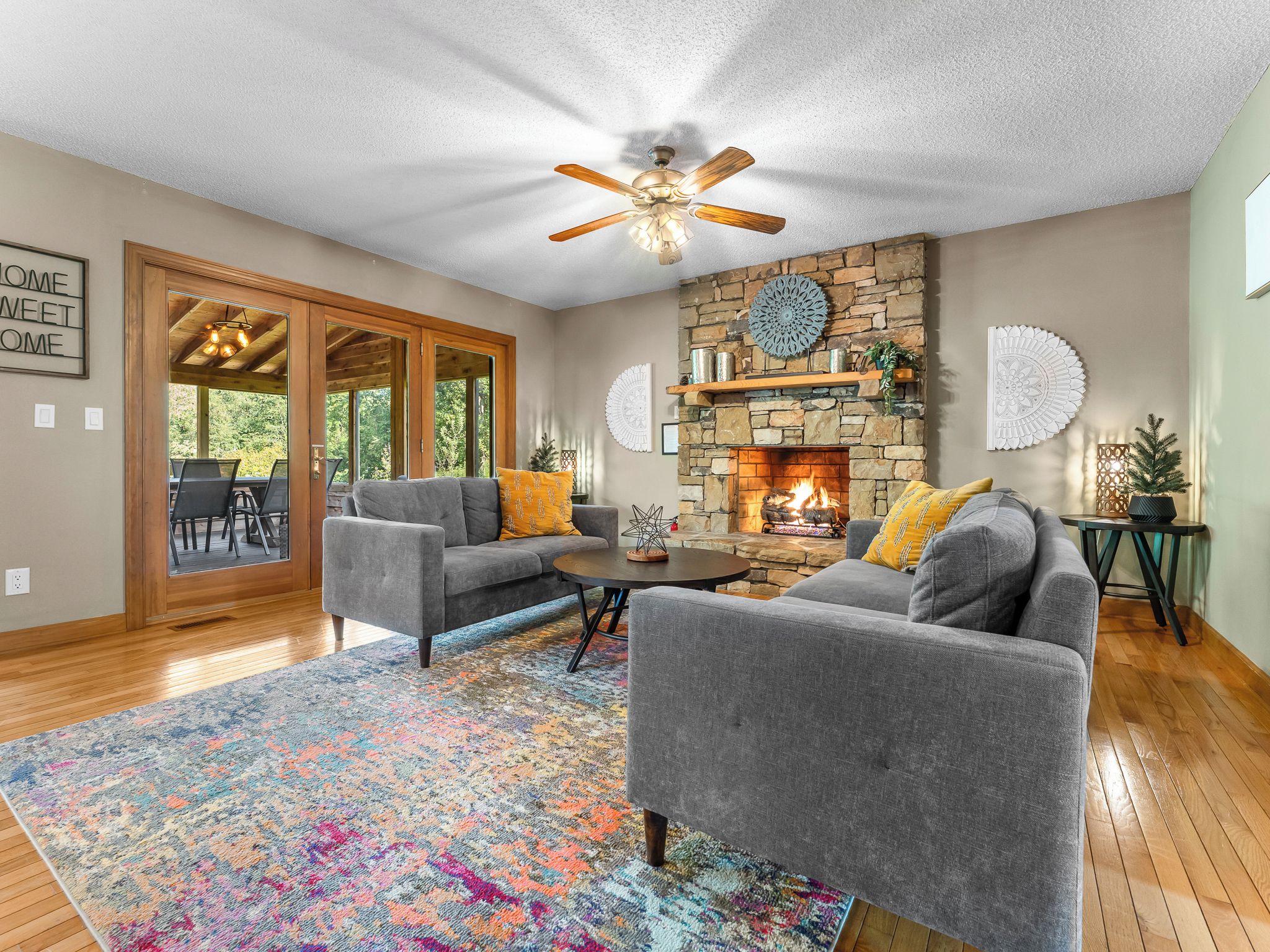 A spacious living room with a stone fireplace, grey sofas, and a colorful rug.