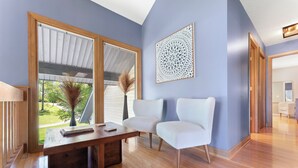 Una habitación moderna con un escritorio de madera, dos sillas blancas, un ventanal con vistas a zonas verdes y un elemento decorativo en la pared.
