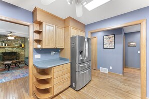 A compact kitchen with wooden cabinets, a stainless steel refrigerator, and a stone fireplace.
