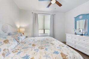 Quarto com cama, cômoda, ventoinha no teto e janela com cortinas.