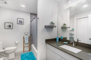 Um banheiro moderno com vaso sanitário branco, chuveiro com cortina listrada, pia com bancada marrom e espelho com prateleira que acomoda uma planta em vaso.