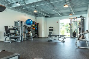 Un gimnasio con diversos equipos de ejercicio, una banca y un espejo grande.
