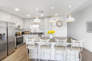 Una cocina moderna con armarios blancos, electrodomésticos de acero inoxidable y una isla central con taburetes de bar.