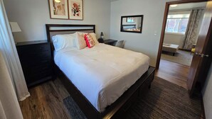 A hotel room with a bed, a nightstand, a lamp, a mirror, and a window with curtains.