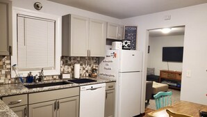 A compact kitchen with white cabinets, a built-in dishwasher, a refrigerator, and a tiled backsplash.