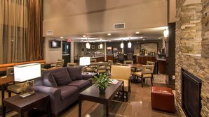 Un hall de hotel con un sofá, mesas, sillas, una chimenea, una zona de bar y un televisor.