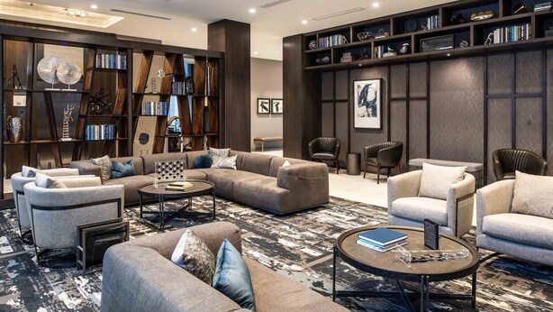 Een moderne woonkamer met een hoekbank, fauteuils, een salontafel en een boekenkast vol boeken en decoratieve objecten.