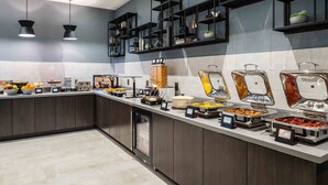 Een moderne buffetopstelling met diverse food stations, een koelkast en decoratieve planken met planten.