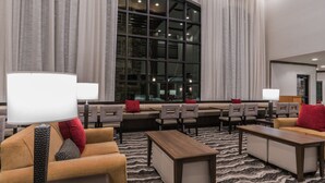 Un hall de hotel con zonas de estar, un ventanal grande y una alfombra estampada.