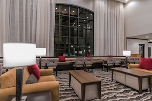 A hotel lobby with seating areas, a large window, and a patterned carpet.