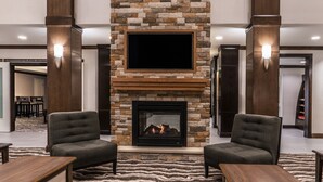 Un hall con chimenea de piedra, dos sillones, un televisor de pantalla plana y una alfombra estampada.