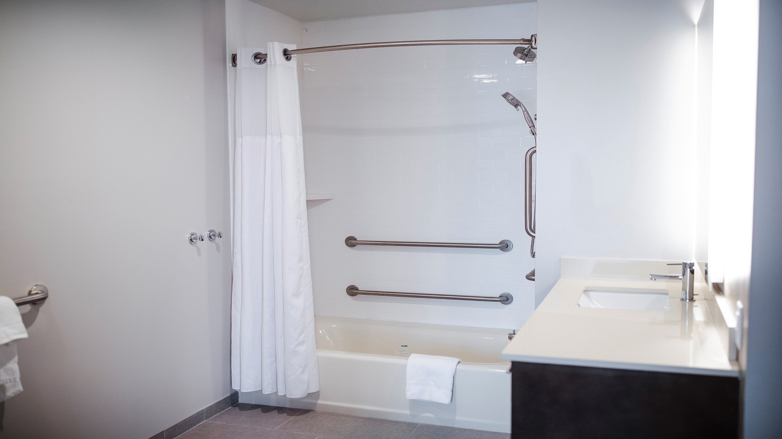 A bathroom with a bathtub, a shower with a handrail, and a sink.