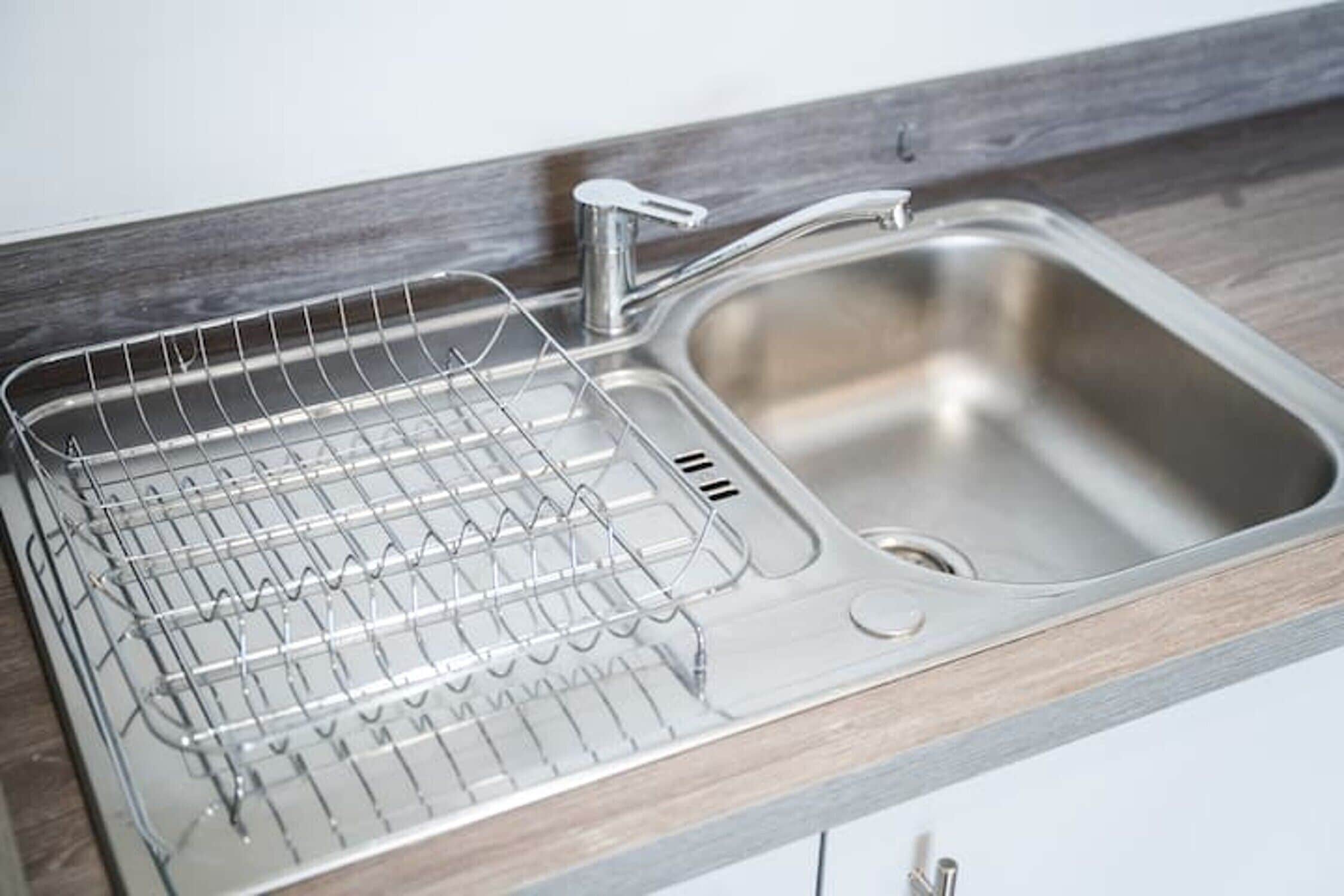 A stainless steel kitchen sink with a wire rack and a faucet.