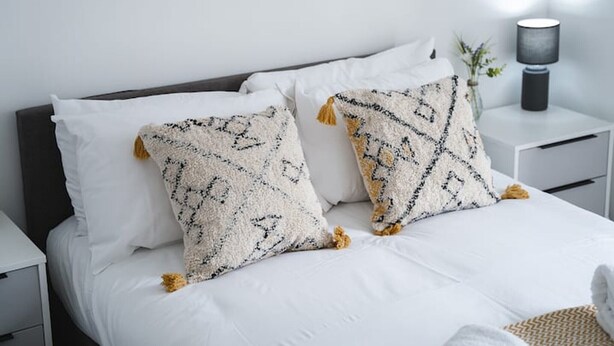 Een net opgemaakt bed met wit beddengoed en twee decoratieve kussens met kwastjes.