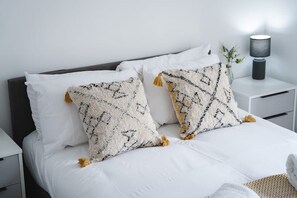 Een net opgemaakt bed met wit beddengoed en twee decoratieve kussens met kwastjes.