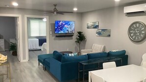A modern living room with a blue sofa set, a dining table with chairs, a flat-screen TV mounted on the wall, and a large wall clock. - Flawless Faith (Redding)