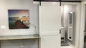 A hallway with a sliding door, a console table with a lamp, and a painting on the wall. - Flawless Faith (Redding)