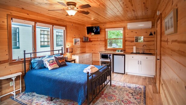 Eine Holzhütte mit Bett, Schreibtisch, Küchenzeile und Deckenventilator.