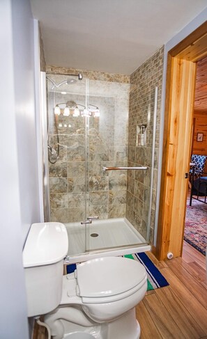 Een badkamer met een douchecabine van glas, een wit toilet en een houten vloer.