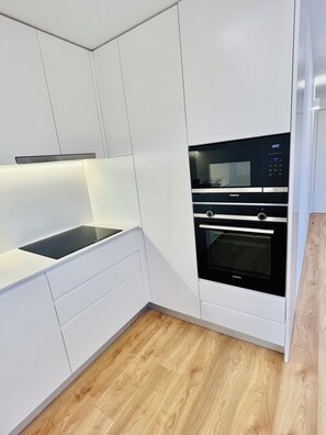 Een moderne keuken met witte kastjes, een inbouwoven en een magnetron.