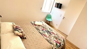 Ein Schlafzimmer mit einem Bett, Kissen, einem grünen Sessel, einem Kleiderschrank und einem Fenster.