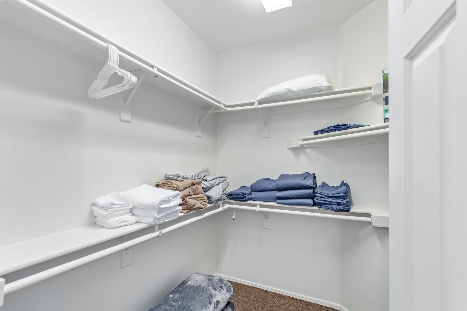 Ein begehbarer Kleiderschrank mit weißen Regalen, gefalteter Kleidung und einer kleinen Sitzbank.