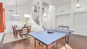 Una habitación amplia con mesa de ping pong, comedor con sillas y una escalera.