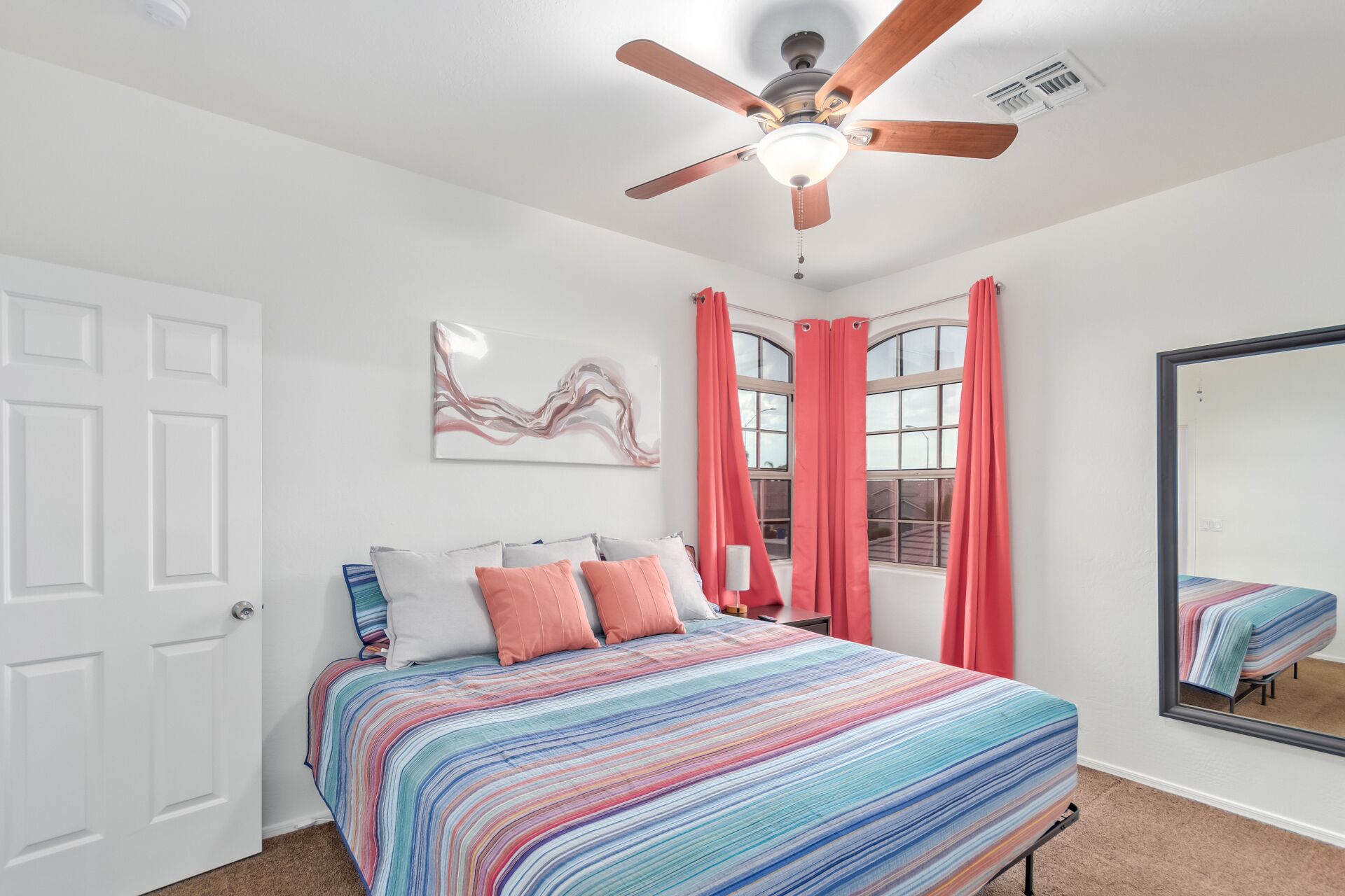 Un dormitorio con cama, ventilador de techo, ventana con cortinas y espejo.