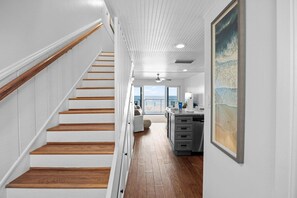 A staircase with wooden steps and white walls leading to a room with a view of the sea.