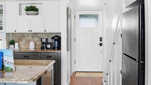 A kitchen with white cabinets, a granite countertop, a coffee maker, and a refrigerator. - Coquina B209 - Crescent Cay. Direct Ocean View (Saint Augustine Beach Florida)