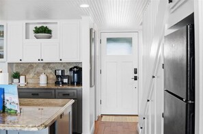 A kitchen with white cabinets, a granite countertop, a coffee maker, and a refrigerator.
