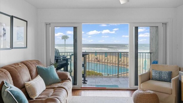Ein Wohnzimmer mit Blick auf den Strand und das Meer durch große Schiebetüren.