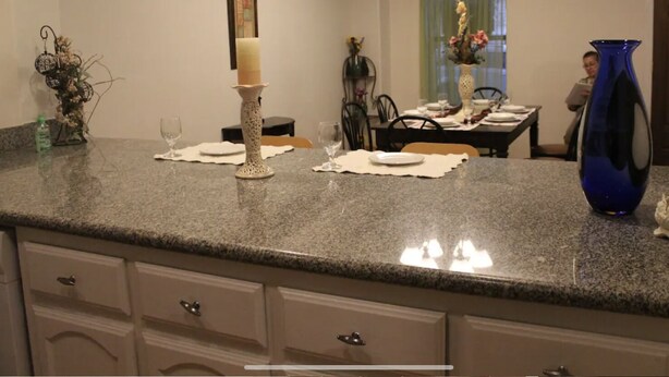 A kitchen with granite countertops, a white cabinet, and a dining area with a table set for two.
