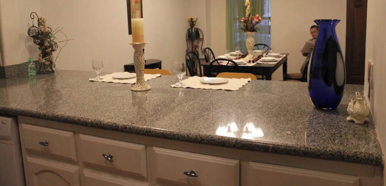 Eine Küche mit Granitarbeitsplatten, einem weißen Schrank und einer Essecke mit Tisch für zwei Personen.