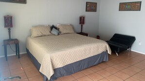 A bedroom with a large bed, two bedside tables, a chair, and three wall-mounted artworks.