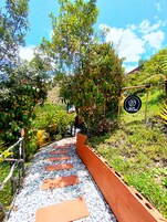 Uma passagem com pedras no caminho serpenteia por um jardim com diversas plantas e uma placa com a inscrição 'AQUA TURQUESA'.