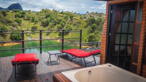 A balcony with a hot tub, two lounge chairs, and a view of a river and hills. - Glamping The Mountain (Guatapé)