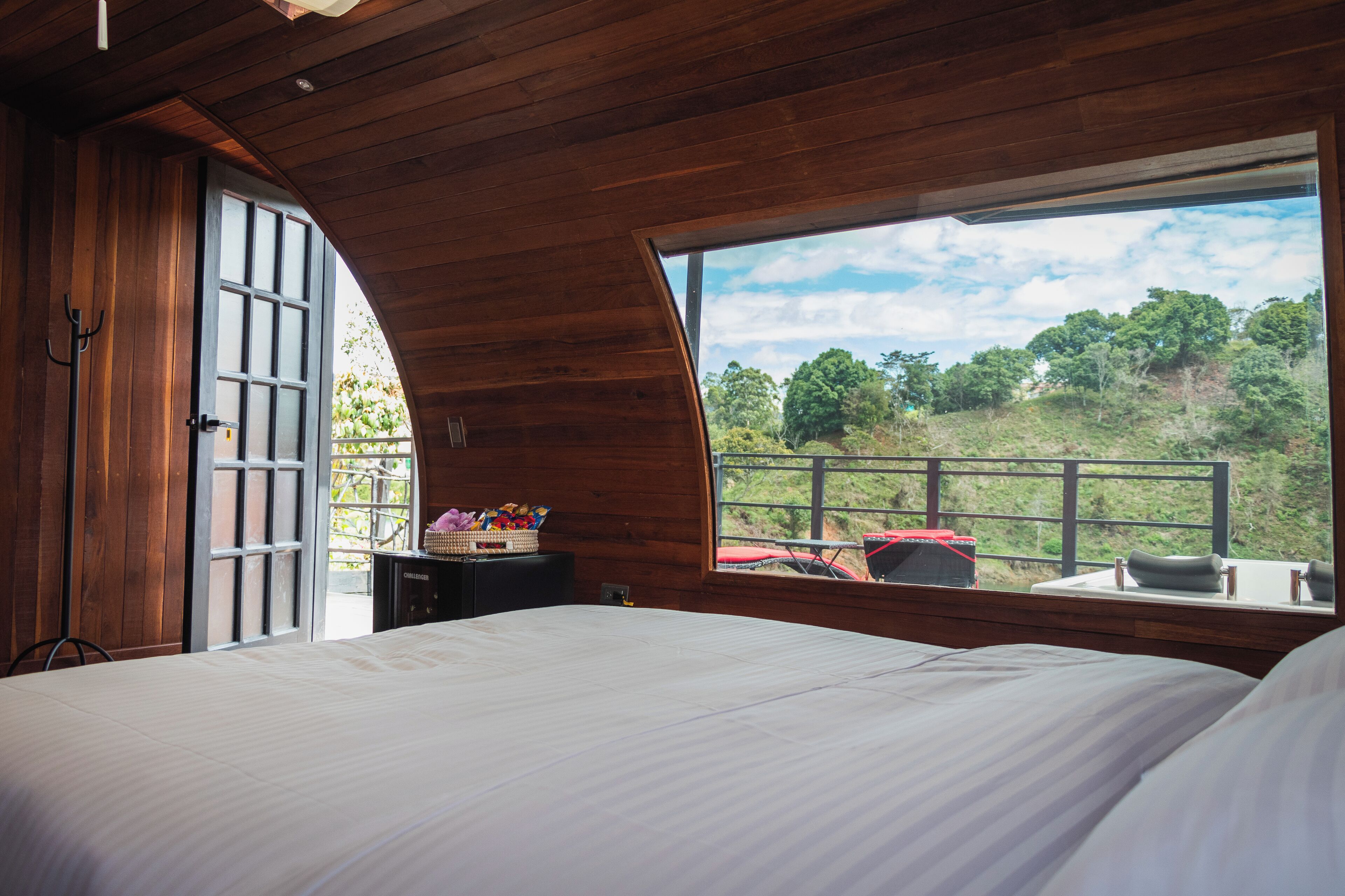 A bedroom with a large bed, a window with a view of a green landscape, and a small table with a basket of items.
