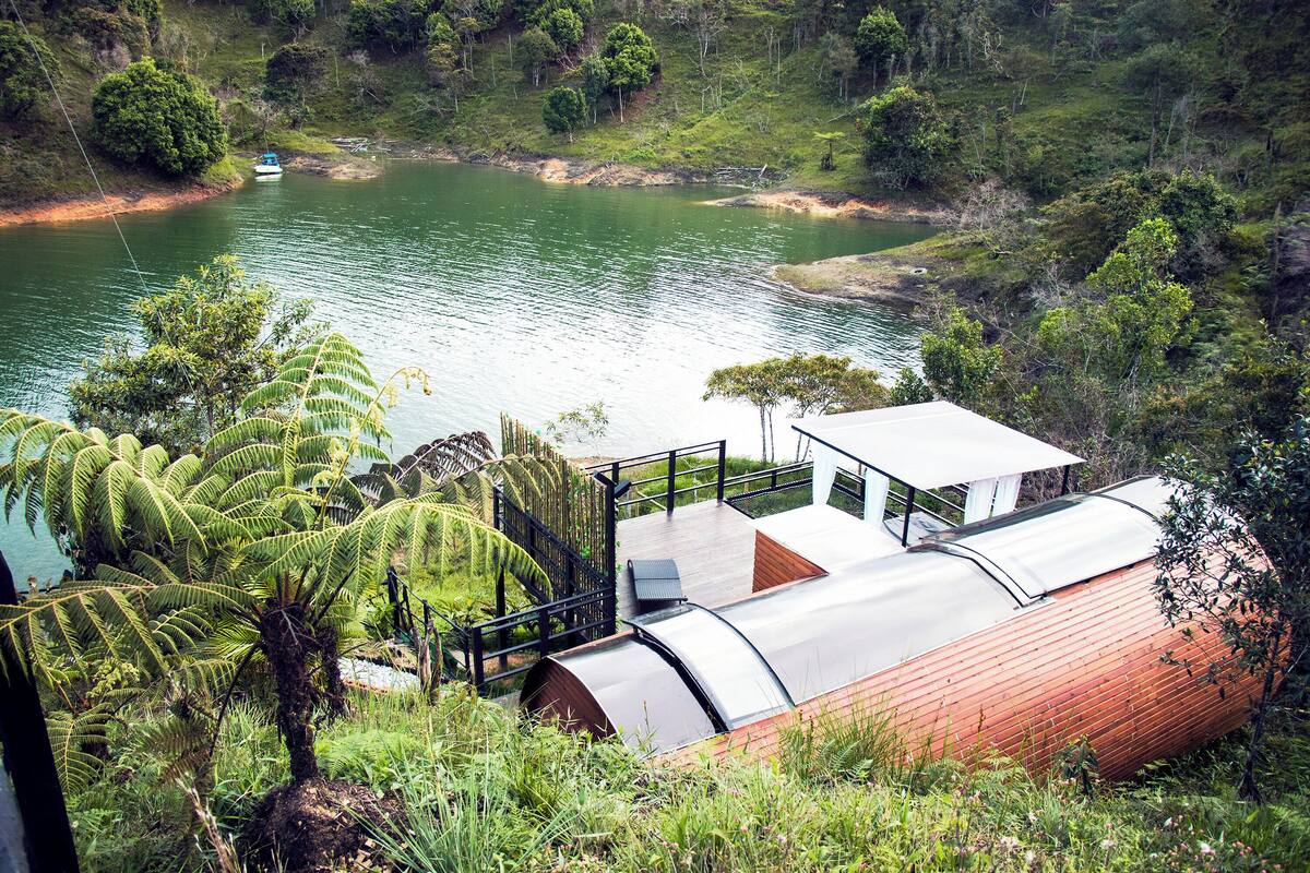 Un bâtiment moderne doté d’un toit incurvé, d’une terrasse en bois et offrant une vue sur un lac.