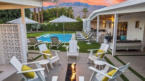 A poolside area with lounge chairs, a fire feature, and a view of mountains.