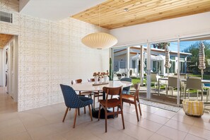 A modern dining area with a round table, wooden chairs, and a hanging light fixture.