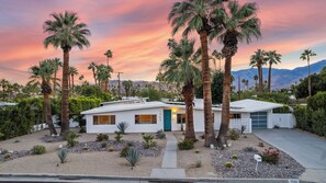 A modern two-story house with a white exterior, surrounded by palm trees and desert landscaping.