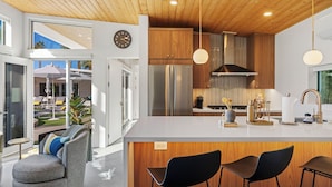 A modern kitchen with a large island, wooden cabinets, stainless steel appliances, and a view to the outdoors. - NEW! Fully remodeled MCM w/mtn views, pool, & large yard! Designed by HGTV star! (Palm Springs)