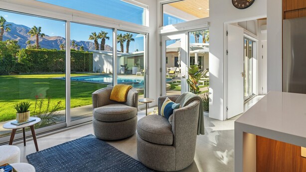 A modern interior with a large sliding glass door leading to a pool, two grey armchairs, and a wooden ceiling. - NEW! Fully remodeled MCM w/mtn views, pool, & large yard! Designed by HGTV star! (Palm Springs)