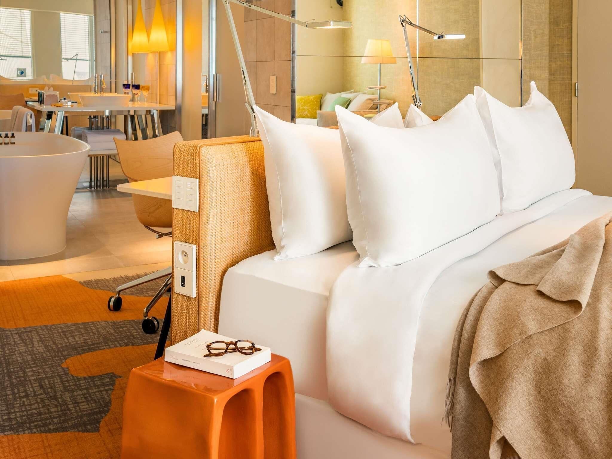 A modern hotel room with a bed, bedside table, and a bathroom visible in the background.