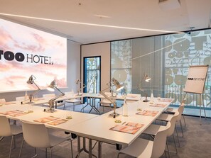 A modern hotel conference room with white tables, chairs, and a large screen displaying 'TOO HOTEL'. - Too Hotel & Spa Paris - MGallery Collection (Paris)