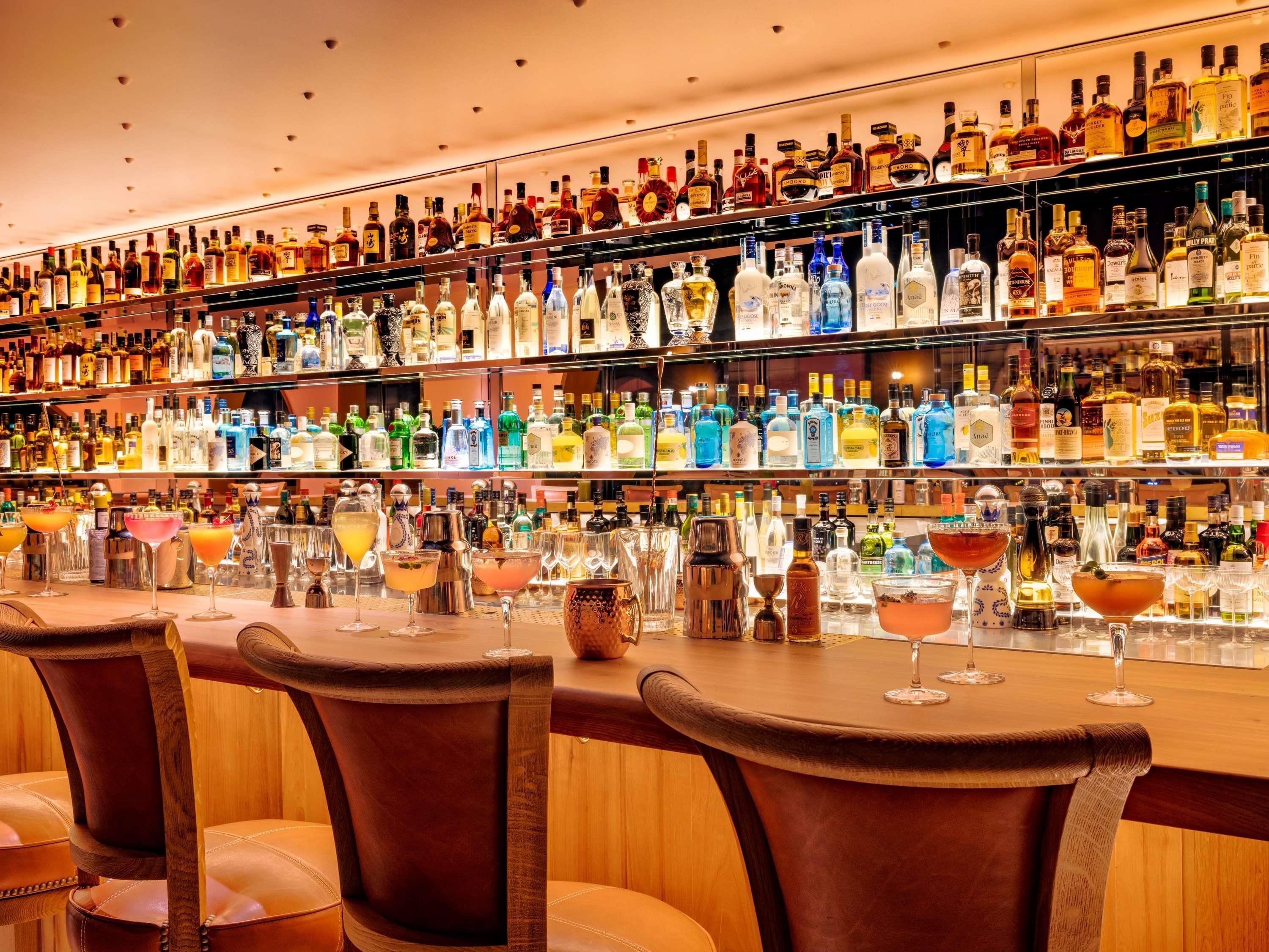 A bar area with multiple shelves of liquor bottles and a variety of glasses on the counter.
