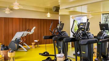 Uma academia com equipamentos de ginástica, piso de madeira e uma parede amarela.